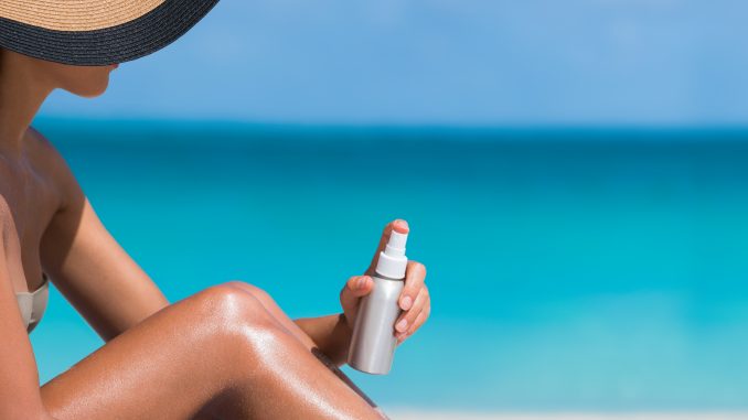 Bikini hat woman applying sunscreen lotion on tanned legs