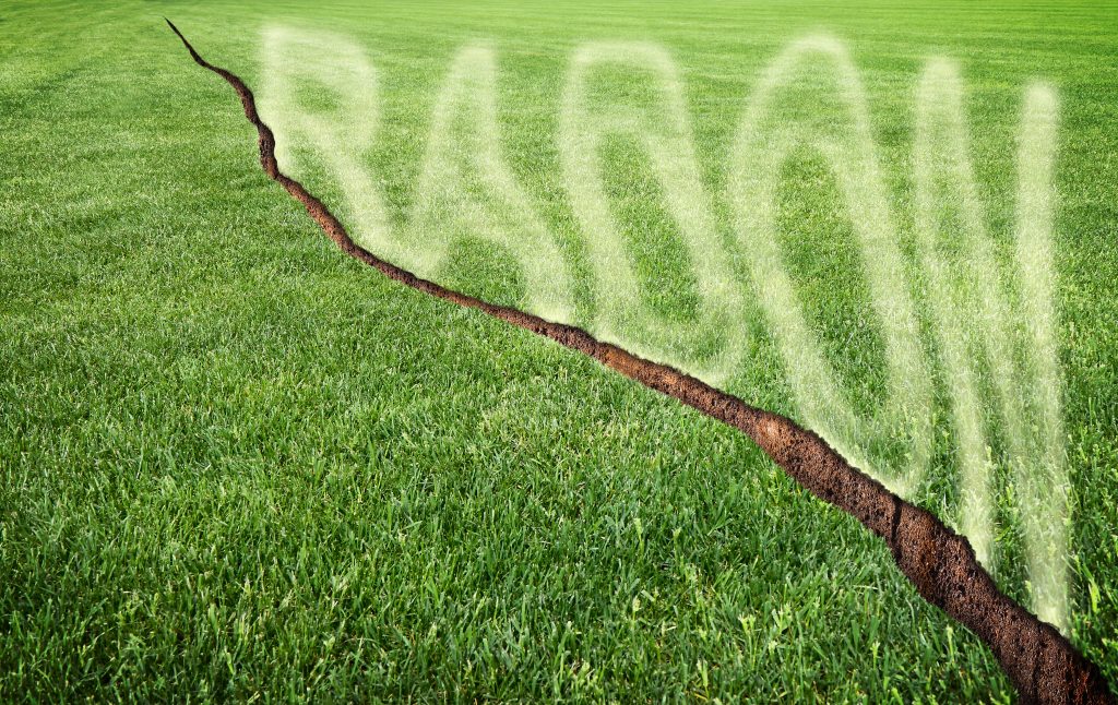 A green mowed lawn with a diagonal crack with radon gas escaping