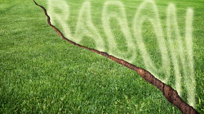 A green mowed lawn with a diagonal crack with radon gas escaping