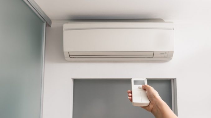 Hand With Remote Control Directed On The Air Conditioner in the room