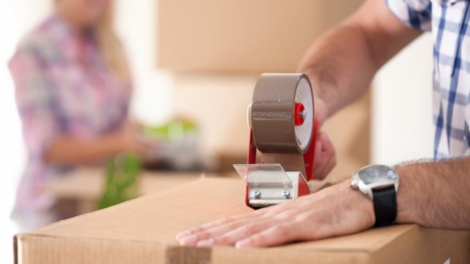 Close up of male hand packing cardboard box, concept moving house